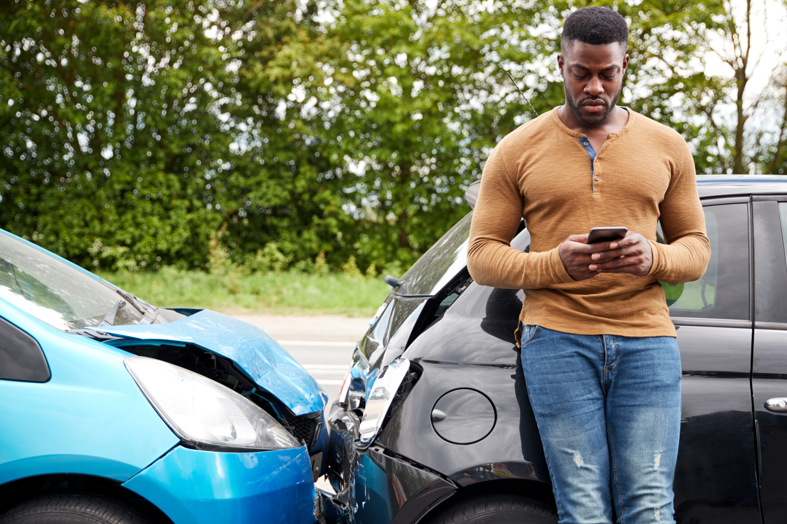 Motorist stands in front of sedan using phone to search if he should get a lawyer for a car accident that wasn't his fault