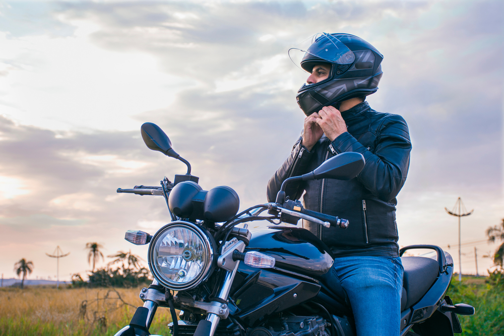 Man abiding helmet law in Alabama sits on motorcycle with nature and sky in background